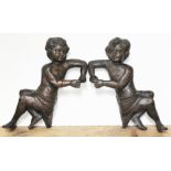 A pair of carved flat back wooden figures, each resting on one elbow and wearing a cloth around