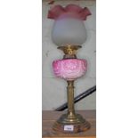 An oil lamp on brass support with wooden base, pink oil reservoir bearing leaf pattern, two coloured
