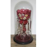 A large red glass drop lustre vase with floral hand painted decoration under glass dome, vase height