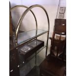 A brass and glass open shelving unit with arched top Catalogue only, live bidding available via