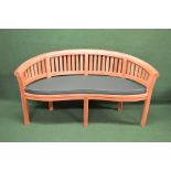 Late 20th century hardwood banana bench having slatted back and seat with seat cushion,