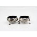 Pair of George III silver salt cellars, raised on three hoof feet, repoussé floral and foliate