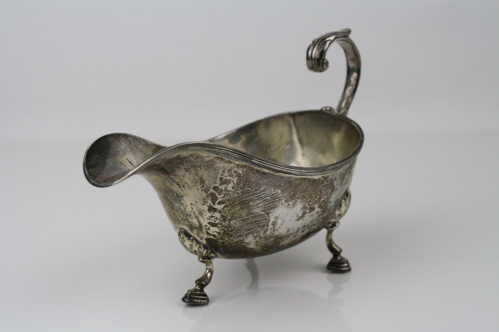 George V silver sauce boat raised on three hoof feet, shell shoulders, ribbed border, scroll handle