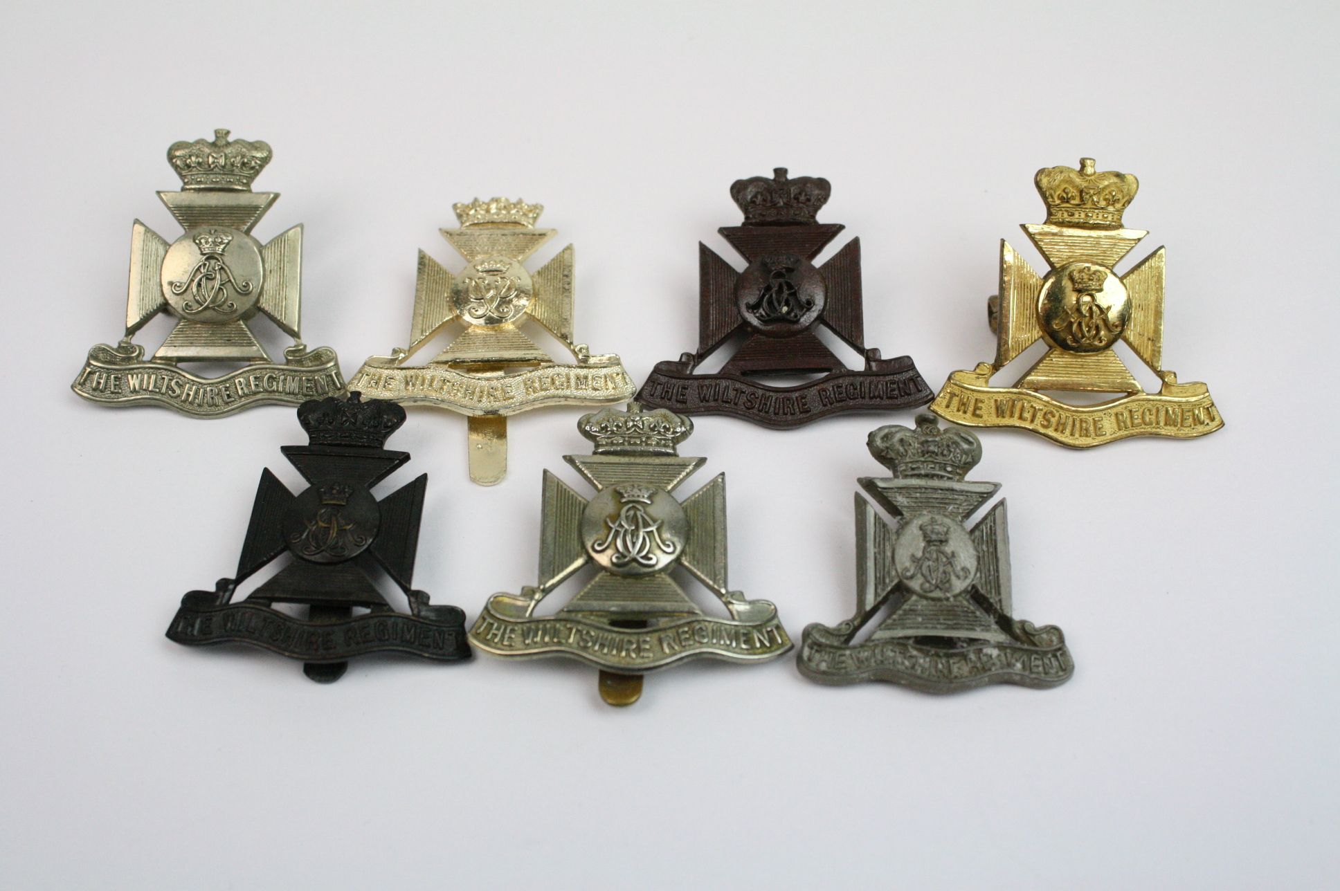 A Collection Of Seven The Wiltshire Regiment Cap Badges To Include A Bronzed, Brass, White Metal,