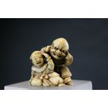 An ivory netsuke of father and son playing, signed, the kneeling father wearing a noh mask, while