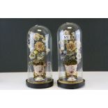 A pair of antique glass domes containiing flower arrangements in vases.