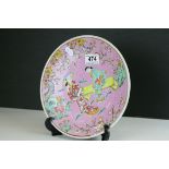An Oriental pink ground plate decorated with figures in a garden.