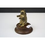 An antique brass match holder in the form of a bear mounted to a wooden plinth.