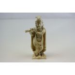 An Indian carved ivory figure standing cross legged playing a flute, h:12cm