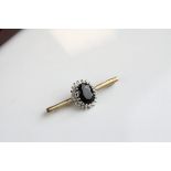Sapphire and diamond cluster 9ct yellow gold bar brooch, the blue-black oval faceted sapphire with