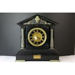 A large slate mantle clock with brass Corinthian columns and mask decorated pediment.