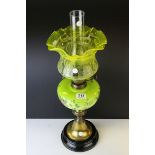 An antique oil lamp with floral green well raised on a brass and black ceramic base,with an art