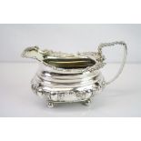 George IV silver cream jug raised on four ball feet, cast flower head, shell and scroll decoration