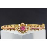 Edwardian style ruby and pearl unmarked yellow gold hinged bangle, the central quatrefoil design and
