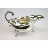 Silver sauce boat, plain polished body raised on three hoof feet, scroll handle with acanthus leaf