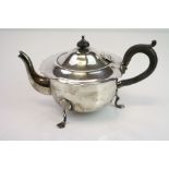 Silver bachelors teapot raised on three feet, ebony handle and finial, ogee style border to the