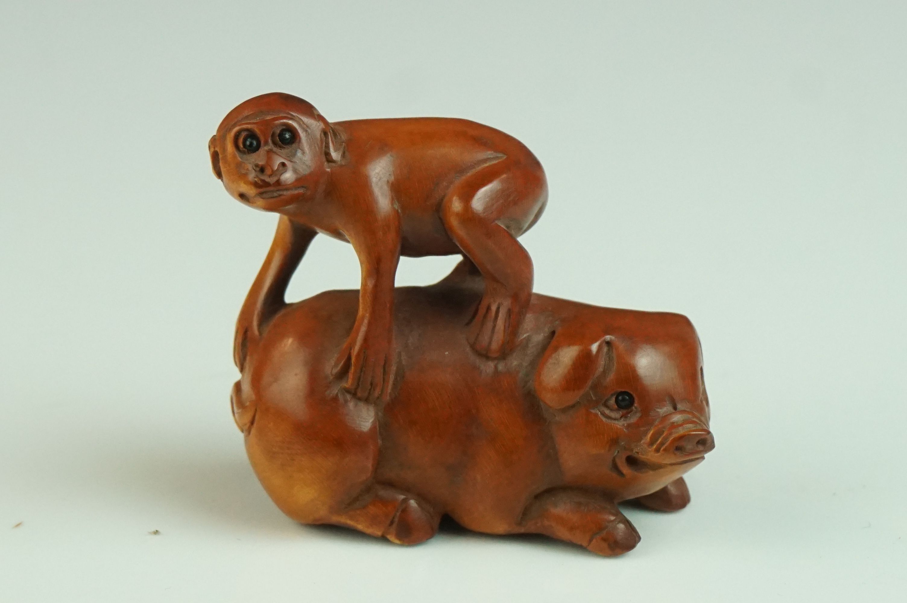 Japanese Carved Boxwood Netsuke in the form of a Monkey stood on a Pig, signed, 5cms long