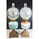 Two antique oil lamps with floral decorated ceramic wells, both with cast iron bases, floral