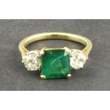 An emerald and diamond dress ring, the square cut central stone, approx 3ct, flanked by bright cut