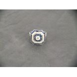 A platinum square shaped ring with chamfered corners, set with a central diamond surrounded by a