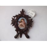 Small porcelain painted panel of a cherub in carved wood easel backed frame