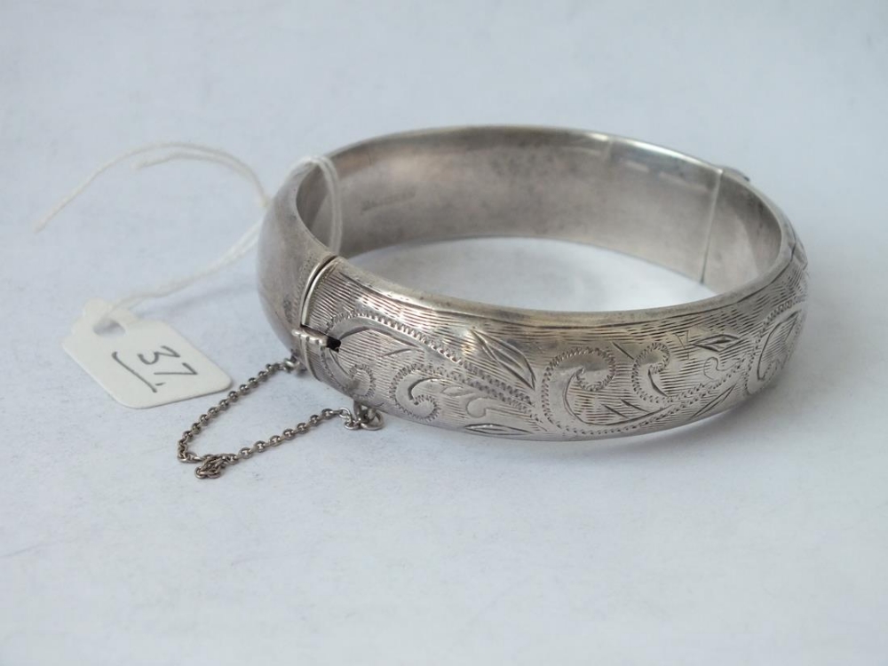 A silver hinged bangle engraved with scrolls