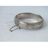 A silver hinged bangle engraved with scrolls