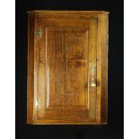 An 18th Century Oak Hanging Corner Cupboard with a fielded panel door flanked by canted sides