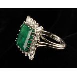 An Emerald and Diamond White Gold Ring. The central emerald cut stone surrounded by 1.