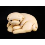 An Edo Period Japanese Netsuke carved as a reclining puppy with inset eyes, holding a shell,