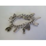 A heavy silver charm bracelet with various silver and white metal charms - approx 81 grams