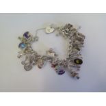 A silver charm bracelet with various silver and white metal charms, approx 65 grams