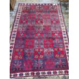 A hand knotted woolen rug with a red field 242cm x 156cm, some patches of wear and fraying to