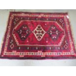 A small hand knotted woolen rug with a red field - generally good condition