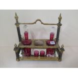 An ornate gilt metal 3 bottle cranberry licquer stand with 2 bottles, a stopper and 3 glasses. One