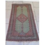 A hand knotted woollen rug with a green field, some overall wear, 200cm x 115cm. Removed from a
