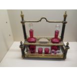 An ornate gilt metal 3 bottle cranberry glass liquor stand with 2 bottles, a stopper and 3