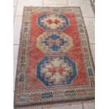 A hand knotted woollen rug with a red field, 210cm x 136cm, some wear. Removed from a Cambridge