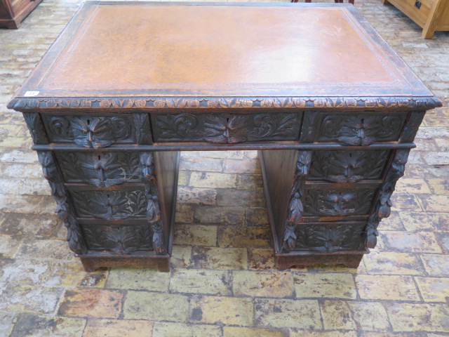 An oak kneehole writing desk with tooled leather top and ornate 'Green Man' carved drawers, 107cm