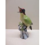 A porcelain model of a green woodpecker on a branch, unsigned, 24cm high, chip to tip of right wing,