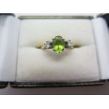 A hallmarked 18ct white and yellow gold ring set with a central oval peridot and two round brilliant