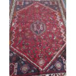 A hand knotted woollen rug with a red field, some wear but colours good