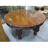 A Victorian circular oak dining table with carved frieze over heavy carved legs and brass castors,