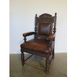 A Victorian oak throne chair with carved detail and brown leather upholstery on four carved legs