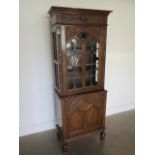 A carved oak 1930s cabinet with a leaded glazed door above a cupboard door on turned feet with a