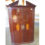 A 19th century mahogany breakfront corner cupboard with two shell inlaid doors enclosing a painted