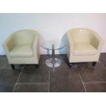 A pair of faux leather cream tub chairs with a glass top coffee table, 49cm x 50cm, some usage marks