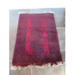 A small hand knotted woollen rug with a red field, 150cm x 100cm, generally good condition