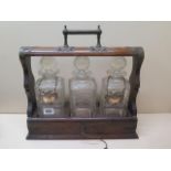 An oak three bottle tantalus with two silver spirit labels, 36cm tall x 37cm wide, small chips to