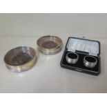A pair of lined silver napkin rings boxed and a pair of silver rimmed wine coasters, no engraving,